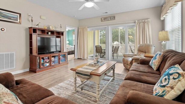 A living room with a television, wooden entertainment unit, brown sofa, and a ceiling fan.