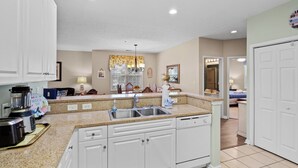 A kitchen with white cabinets, a granite countertop, a double sink, and a chandelier.