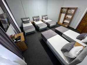 Habitació d'hotel amb quatre llits individuals, un armari de fusta i una petita taula amb un ram de flors.