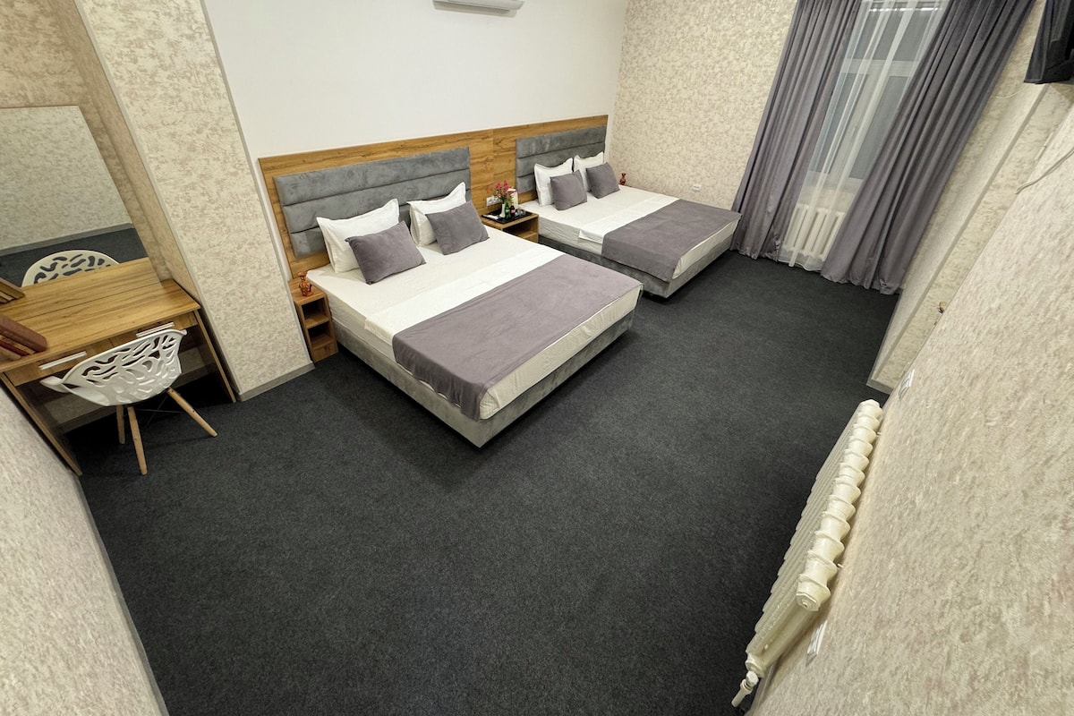 A hotel room with two beds, a desk, a chair, and a window with curtains.