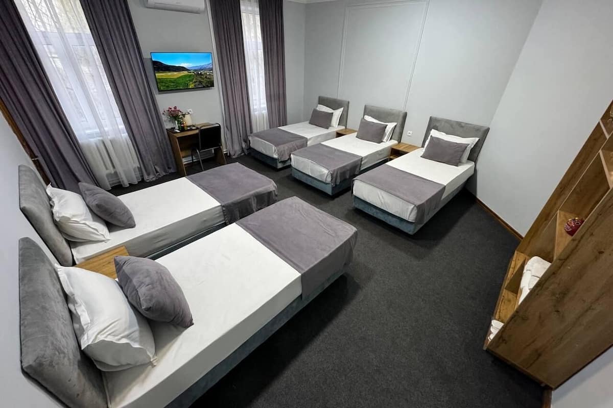 A modern hotel room with four single beds, a sofa bed, a TV, and a small table with a vase.