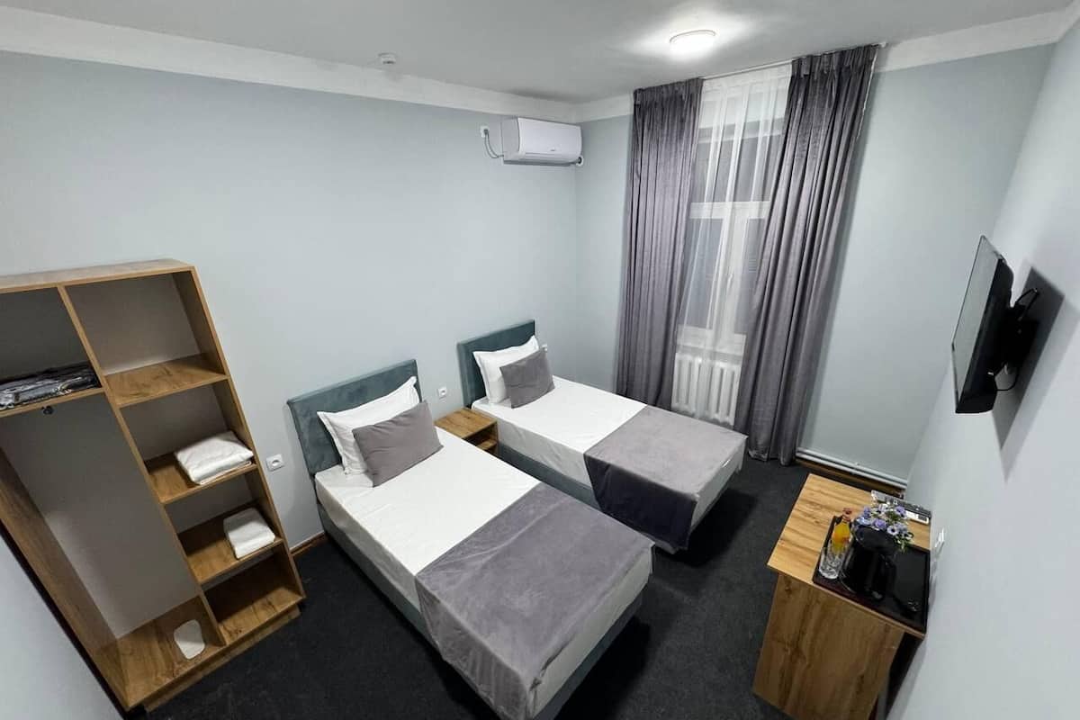 A hotel room with two single beds, a wooden wardrobe, a small desk with a chair, and a TV mounted on the wall.