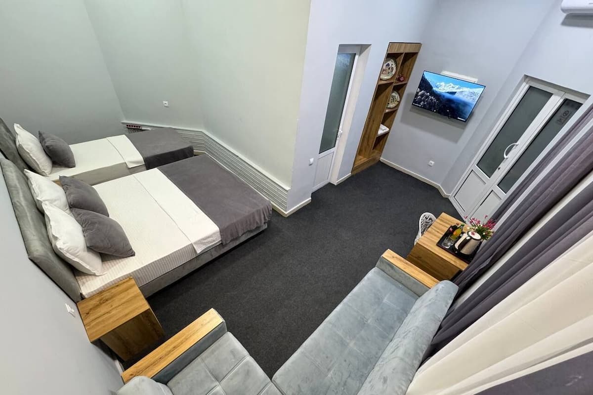 A compact hotel room with a bed, a sofa, a small table, and a TV mounted on the wall.