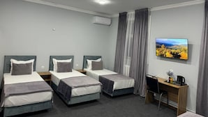Ein Hotelzimmer mit drei Einzelbetten, einem Schreibtisch mit Stuhl, einem Flachbildfernseher und einer Klimaanlage.