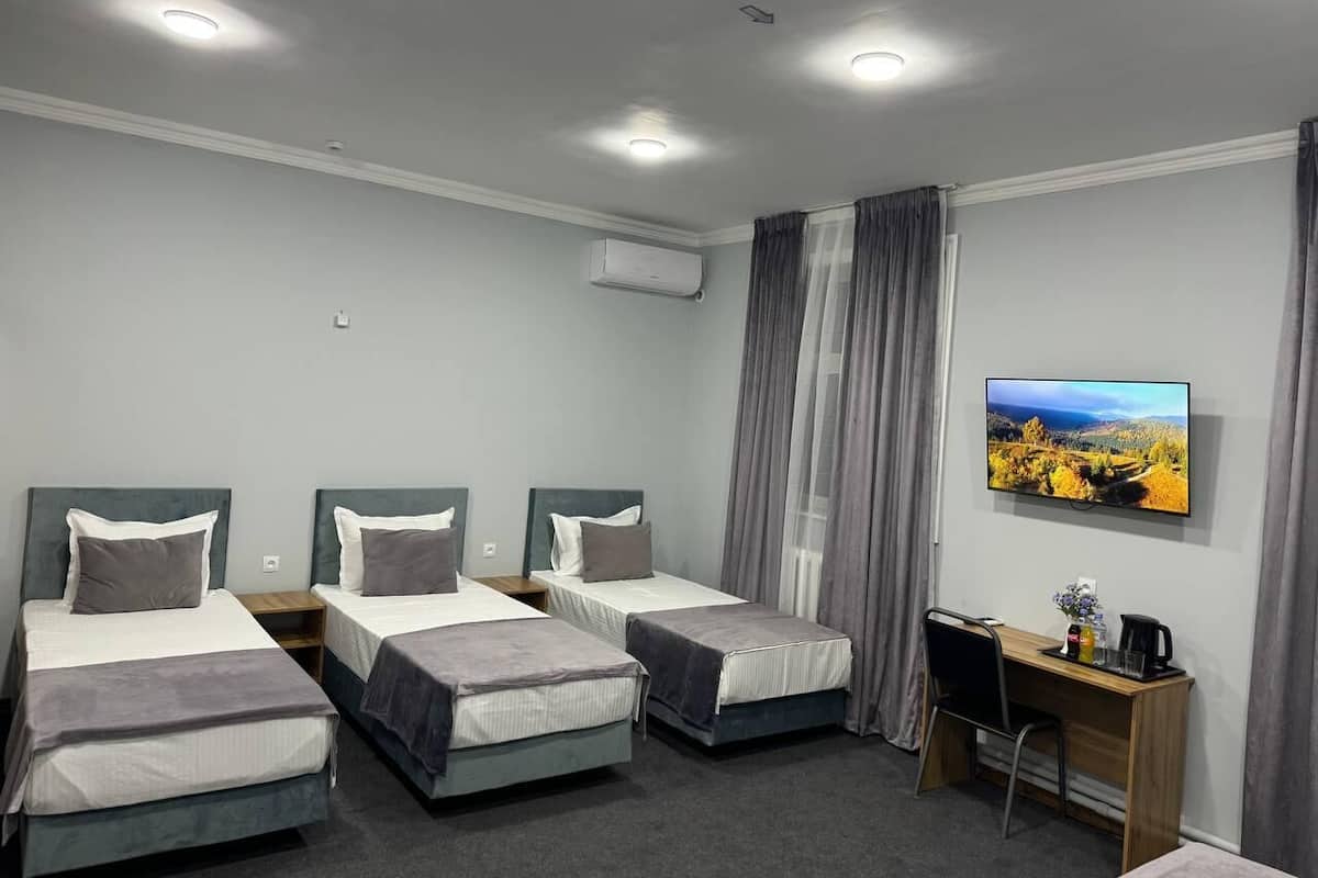 A hotel room with three single beds, a desk with a chair, a flat-screen TV, and an air conditioning unit.