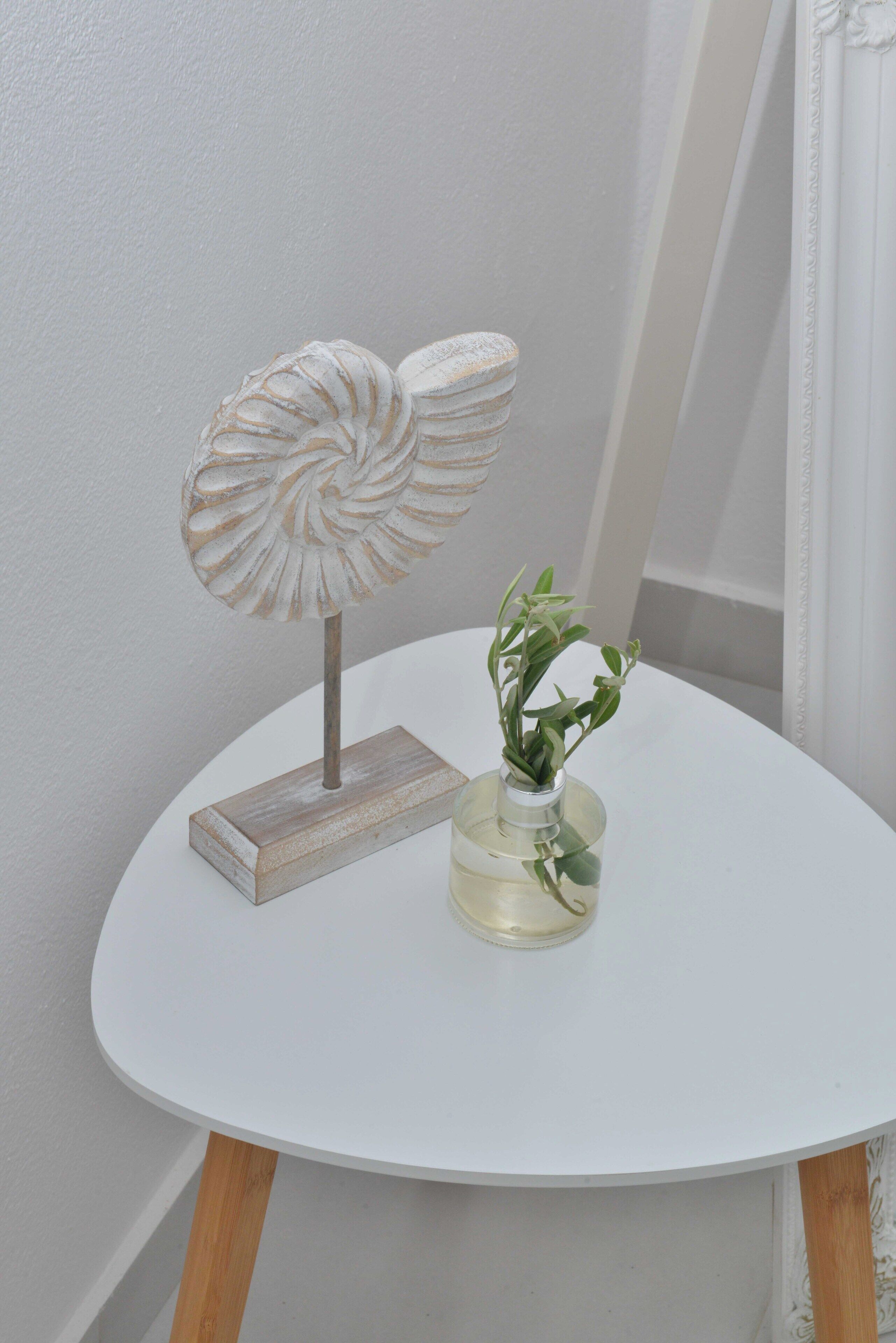 A white round table with a decorative metal piece and a glass vase with a plant.
