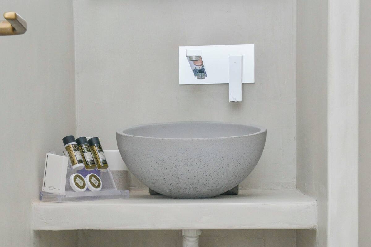 A bathroom with a gray speckled sink, a mirror, and a shelf with towels and toiletries.