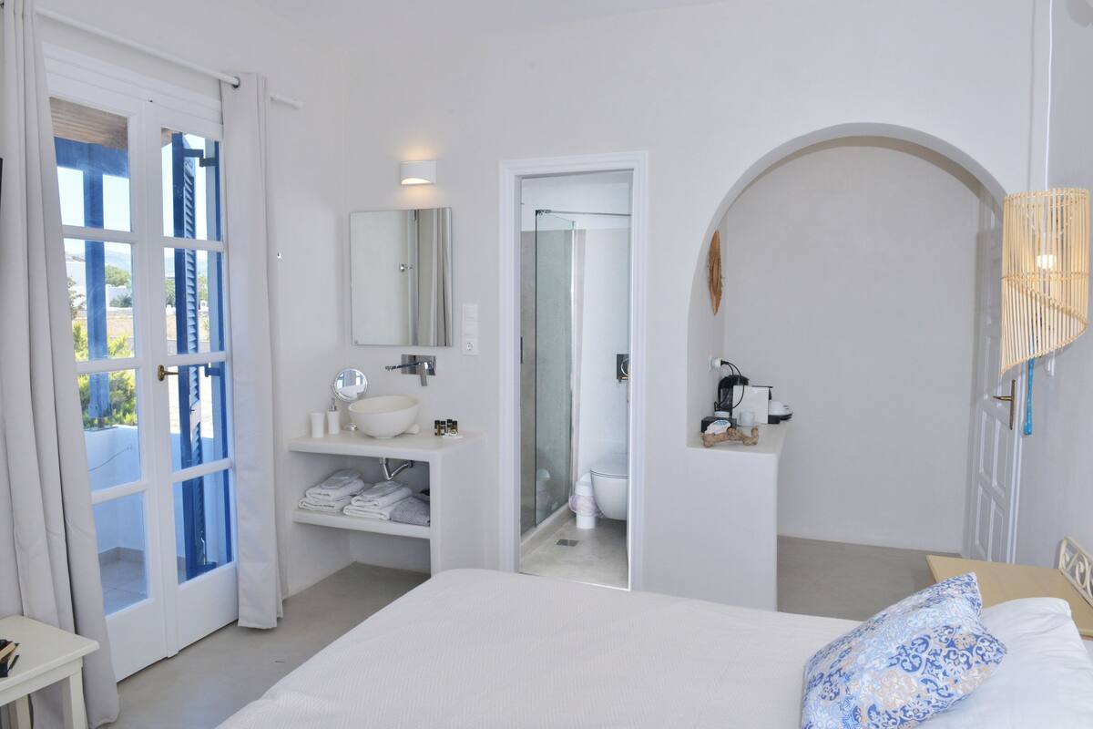 A bedroom with a bed, a bathroom with a sink and mirror, and a shower.