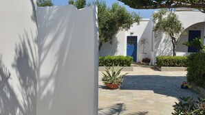 Pátio com edifícios brancos, uma porta azul e plantas em vasos.