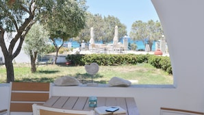 Vista de varanda com mesa e cadeiras, dando para um jardim com árvores e uma vista distante do mar.