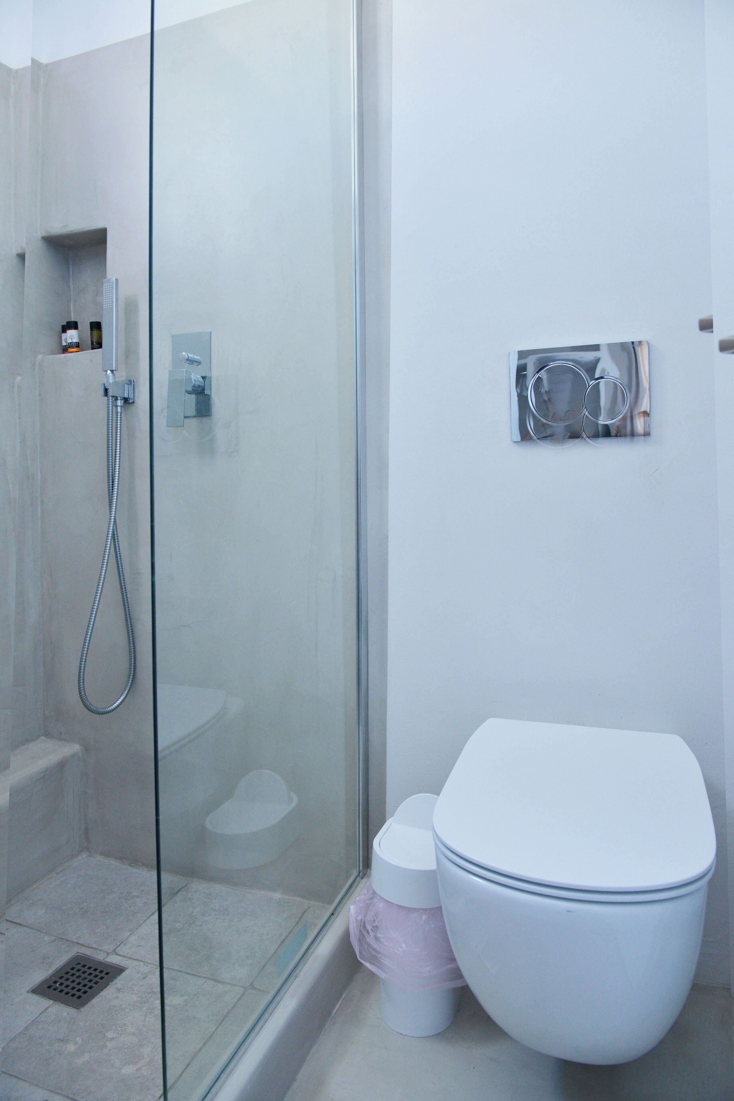 Un baño moderno con ducha de vidrio, inodoro blanco y un pequeño cubo de basura.