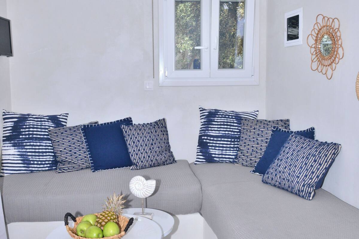 A modern living room with a sofa set, a small table with a fruit basket, and a hanging light fixture.