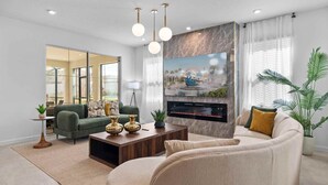 A modern living room with a large flat-screen TV mounted on a marble wall, a fireplace, and a comfortable seating area with a sofa and armchairs. - 2315  Amazing house 6/5 W/Pool Solara Resort (Kissimmee)