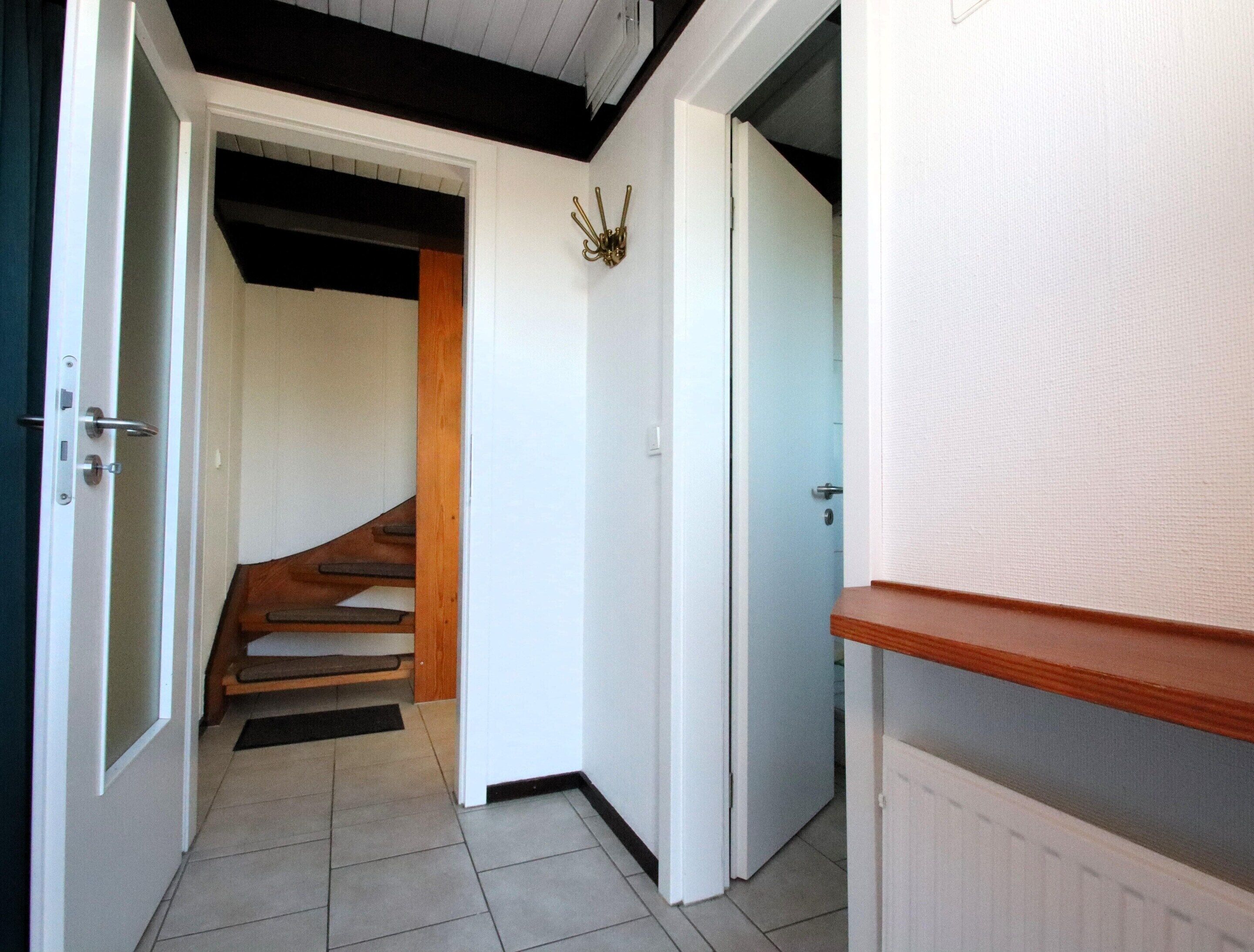 Un pasillo con escalera de madera, paredes blancas y un radiador.