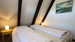 A bedroom with two beds, a painting on the wall, and a nightstand with a lamp. - Nurdachhaus in Burhave (Butjadingen)