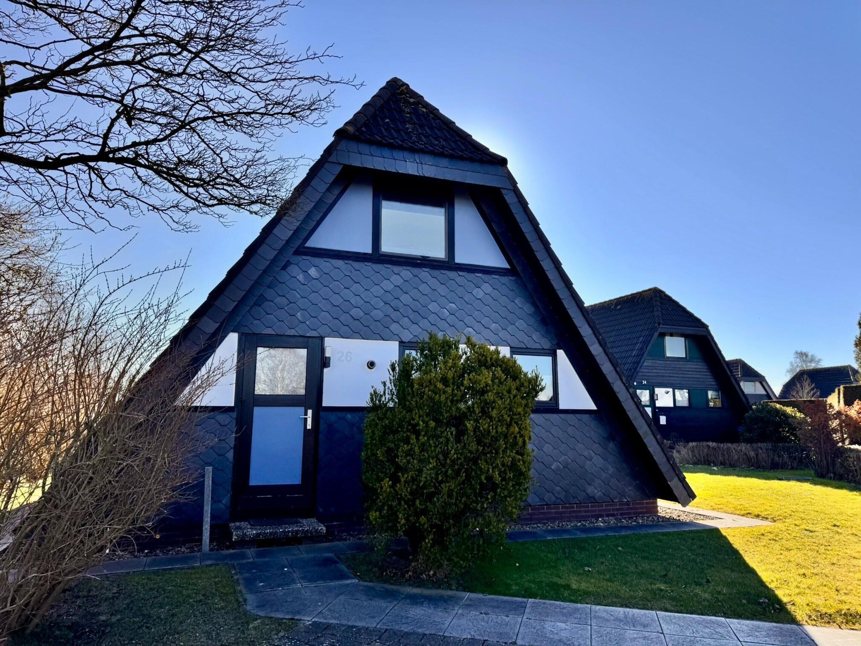 A modern, triangular-shaped house with a dark roof, white walls, and a visible number '26' on the front.
