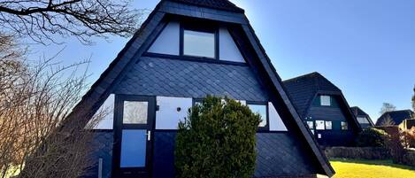 A modern, triangular-shaped house with a dark roof, white walls, and a visible number '26' on the front.