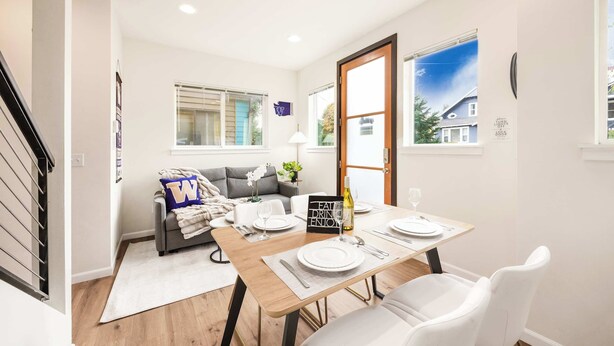 A dining area with a wooden table set for four, a sofa, and a window with blinds.