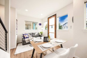 Een eetgedeelte met een houten tafel voor vier personen, een bank en een raam met zonwering.