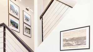 A staircase with a metal railing, wooden steps, and framed pictures on the walls.