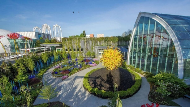 Een modern gebouw met een glazen gevel, omringd door aangelegde tuinen met diverse planten en beelden.