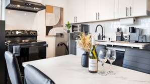 A modern kitchen with white cabinets, a black stove, and a dining table with a vase of dried flowers and wine glasses. - Modern 2BR • Near DT + Stadiums • Parking (Seattle)