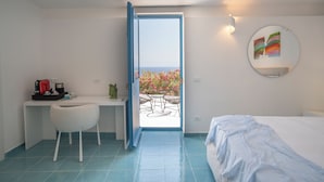 Un dormitorio con cama, escritorio y silla, una mesita con sillas, y vistas a un balcón lleno de flores.