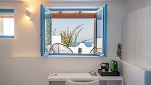 Una habitación con ventana que ofrece una vista panorámica, un escritorio blanco con silla, y una mesita con una taza y un hervidor verde.