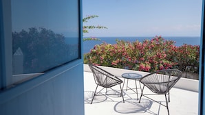 Un balcón con dos sillas y una mesa, con vistas a un jardín de flores rosadas y al mar.