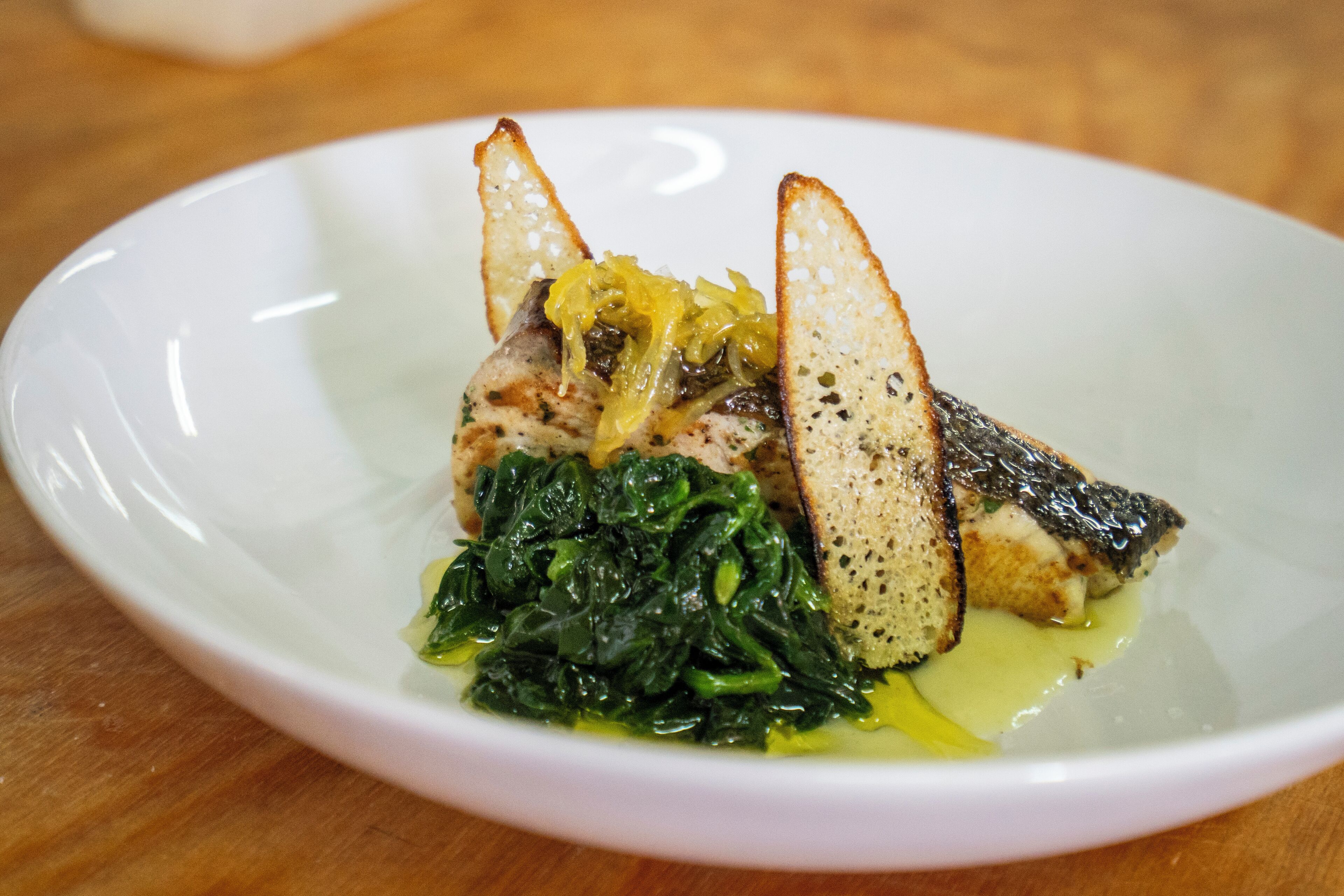 Une assiette blanche contenant un morceau de poisson, une tranche de pain et des légumes verts.