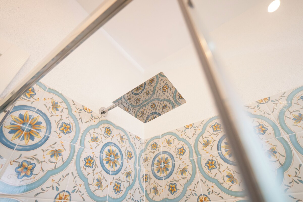 A ceiling with intricate floral tile patterns and a visible showerhead.