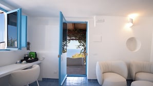 Una habitación con un escritorio blanco, una puerta con marco azul que da a un balcón y dos sillas color beige.