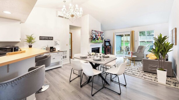 A modern kitchen with a coffee bar, dining area with white chairs, and a living room with a sofa and a plant.