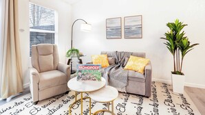 A living room with a sofa, armchair, and a coffee table. There is a Monopoly board game on the table.