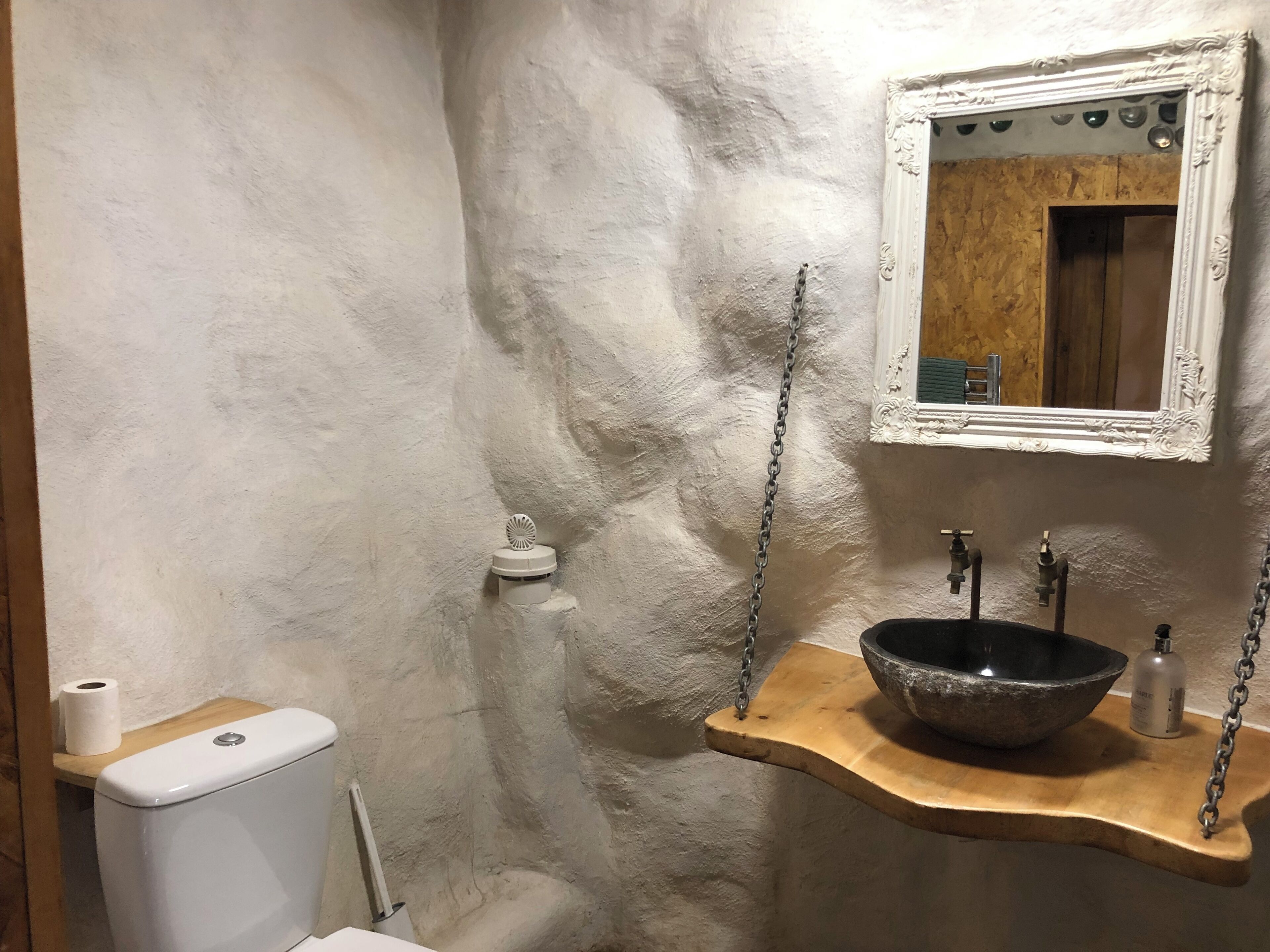 Kylpyhuone, jossa on wc, pesuallas, peili ja puinen hylly.