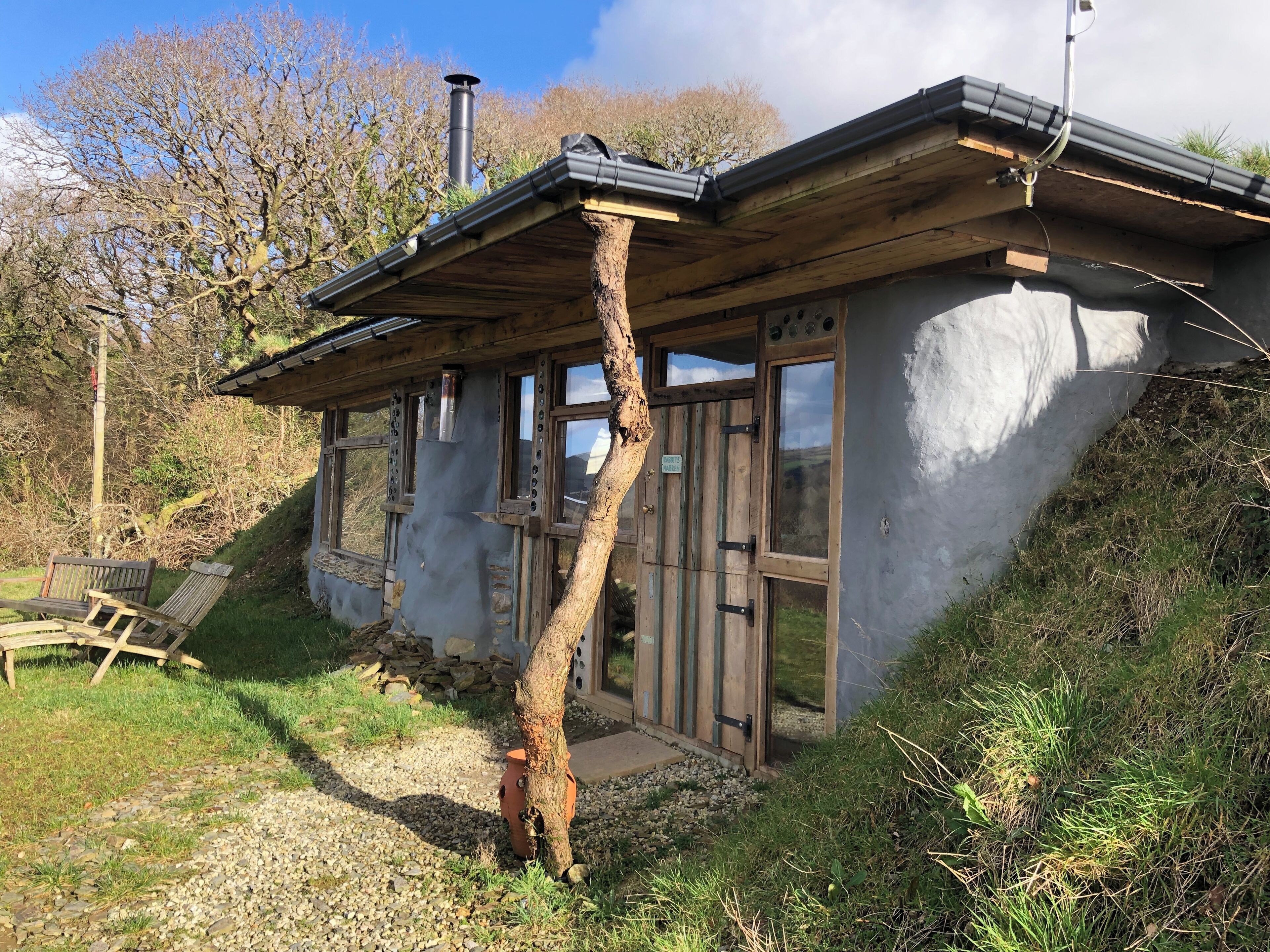 Una cabaña rústica con techo inclinado, ventanas grandes y chimenea.