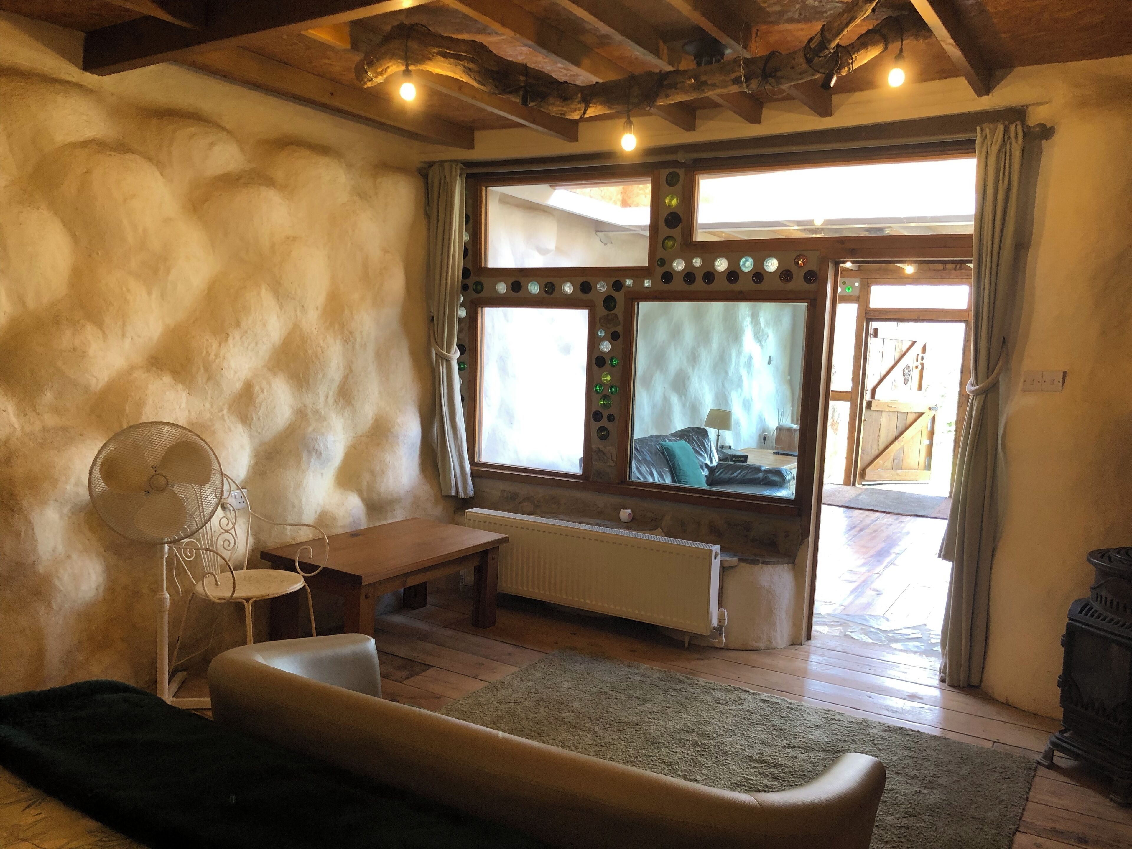 A cozy room with a large window, a radiator, a wooden table, a sofa, and a fan.