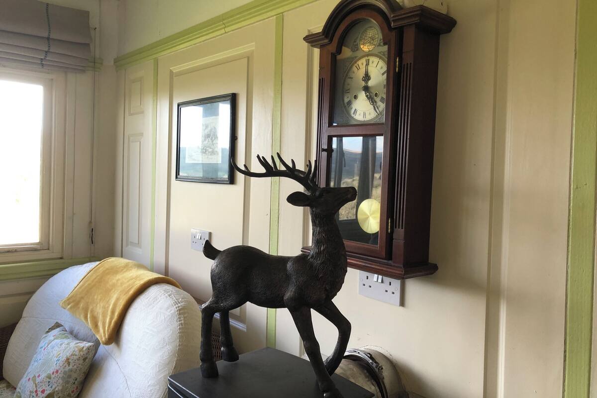 Una habitación con un reloj grande en la pared, un cuadro enmarcado y una estatua de ciervo.