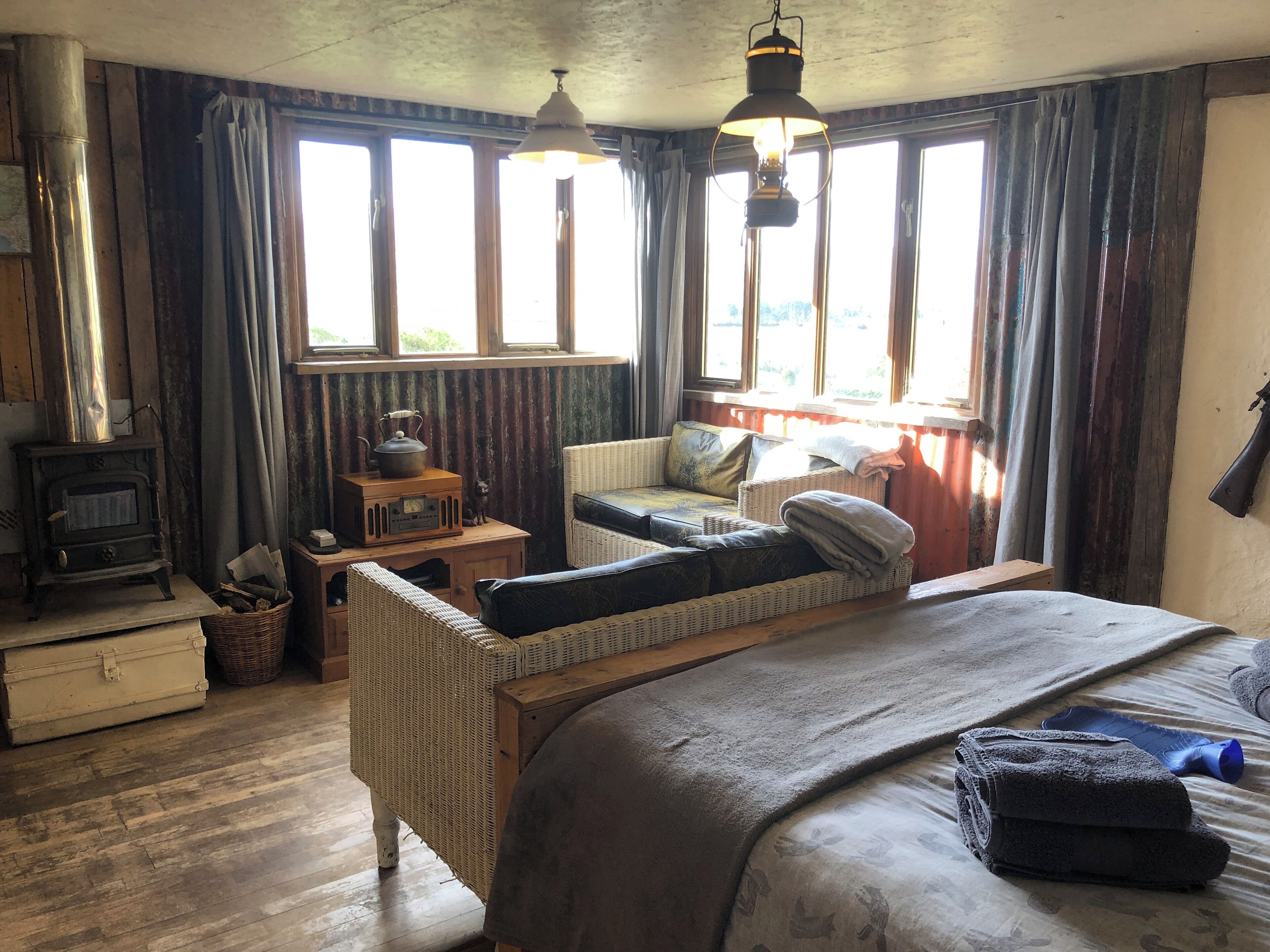 Ein gemütliches Zimmer mit einem großen Bett, einem Korbsessel, einem kleinen Tisch mit einem Radio und einem Kamin.