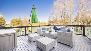 Une terrasse dotée de meubles en osier, d’un parasol vert et offrant une vue sur des arbres et une maison.