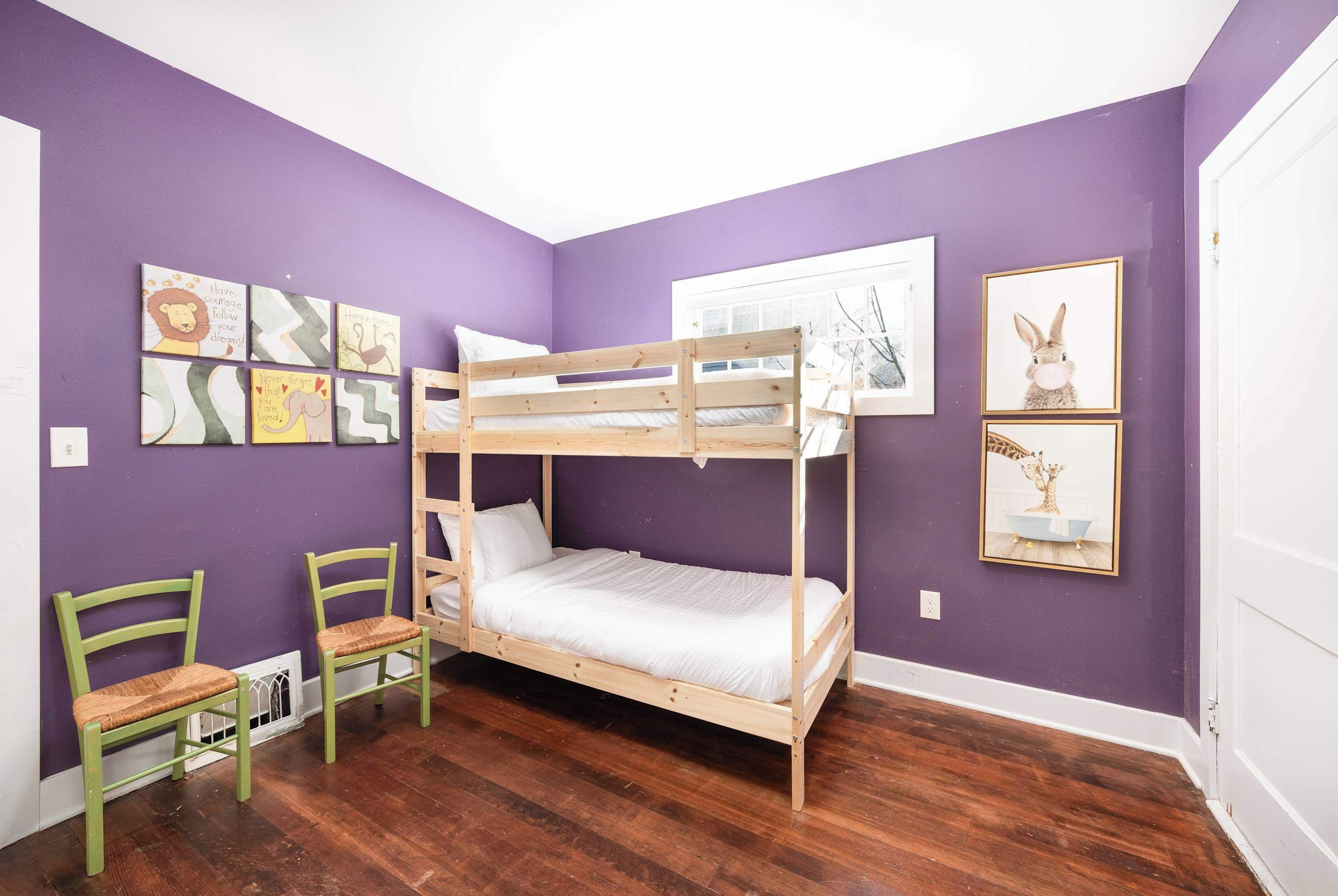 A room with a bunk bed, two chairs, and artwork on the walls.