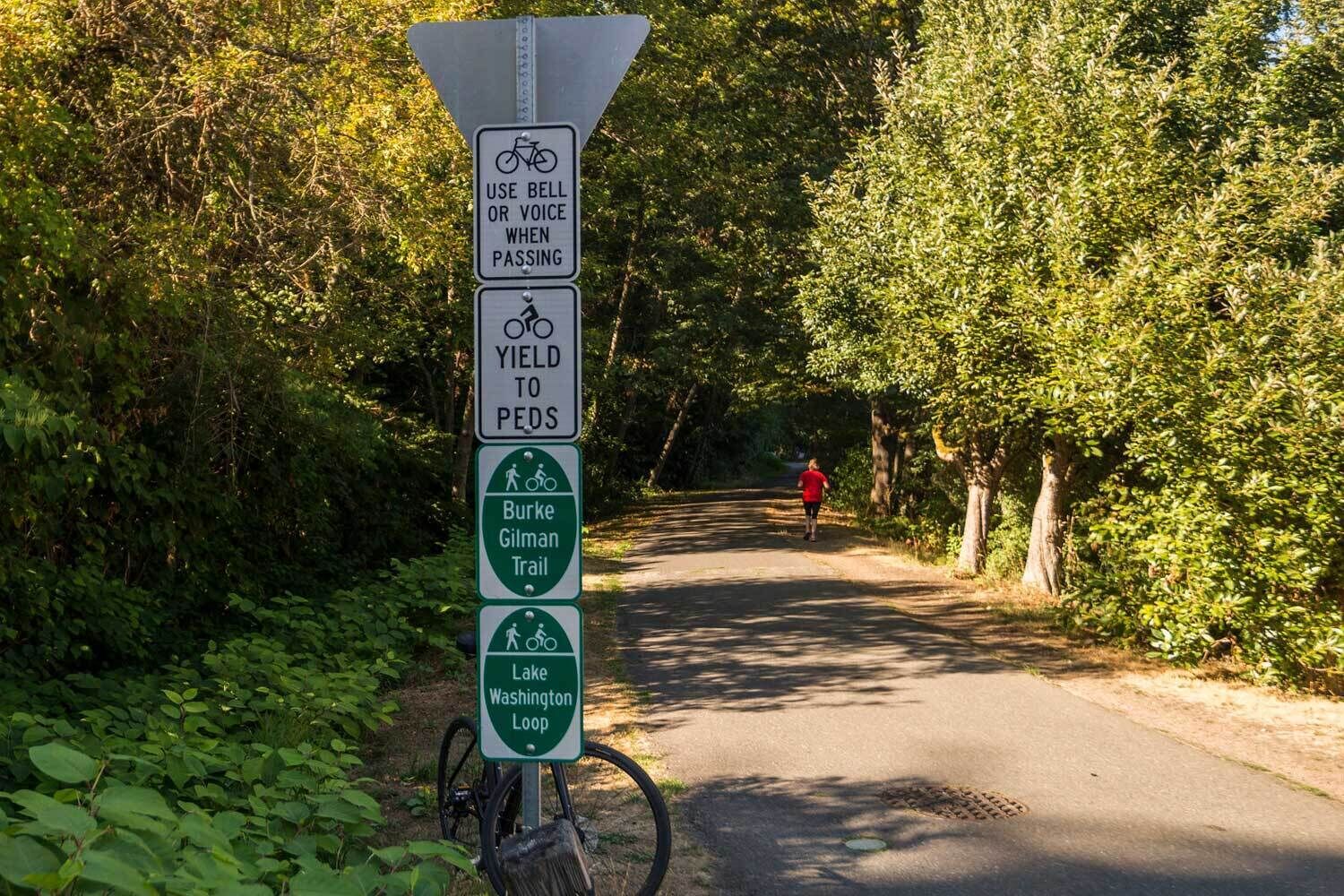 A directional sign for the Burke Gilman Trail and Lake Washington Loop, advising cyclists to use a bell or voice when passing and to yield to pedestrians.