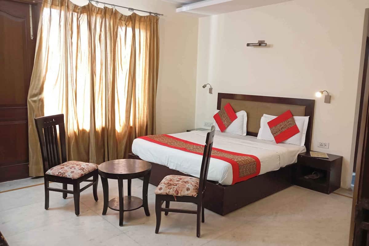 A hotel room with a bed, two chairs, a small table, a nightstand, and a curtain.