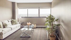 A modern living room with a sofa, a glass coffee table, a lamp, and a large window with a view. - Chic 1-bedroom apartment with fitness room and AC in vibrant Houston (Houston)