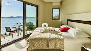 A hotel room with a bed, a small table with two wine glasses, a chair, and a view of the sea through large glass doors. - Beach Villa Smile with private pool (Barbati)