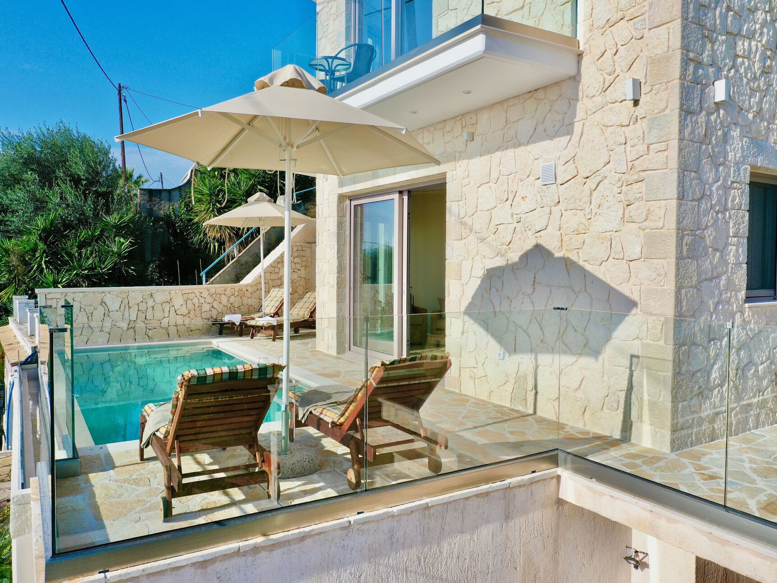 A poolside area with lounge chairs, a glass balustrade, and a stone building facade.