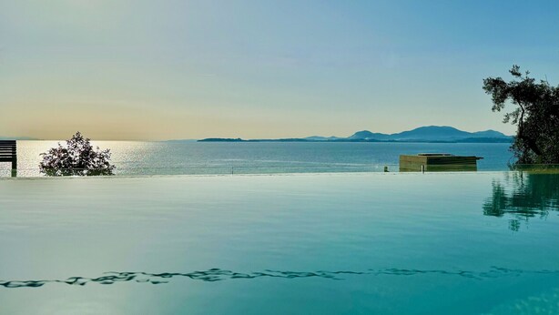 A clear view of a swimming pool with a bench and a small structure, surrounded by calm water and distant mountains. - Beach Villa Smile with private pool (Barbati)