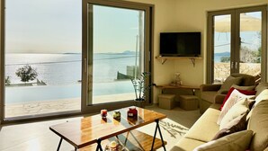 A living room with a large sliding glass door offering a sea view, a flat-screen TV mounted on the wall, and a cozy seating area with a sofa and armchairs. - Beach Villa Smile with private pool (Barbati)