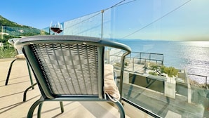A balcony with a chair and a glass of red wine, overlooking a body of water and a distant coastline. - Beach Villa Smile with private pool (Barbati)