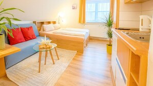 Et lille værelse med seng, et lille bord, en sofa, et vindue og et tekøkken.